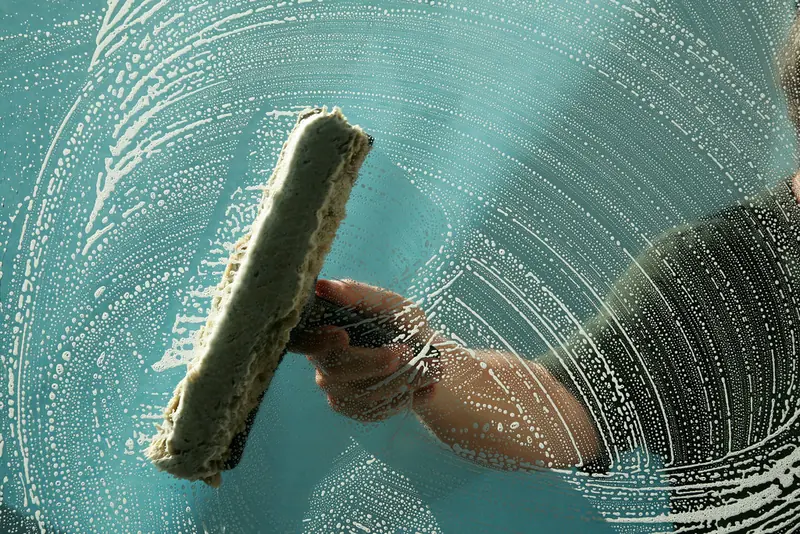 A window cleaner working a squeegee through soapy glass